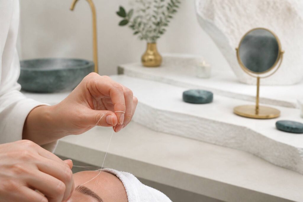 Mains pratiquant l'épilation au fil au niveau d'un sourcil