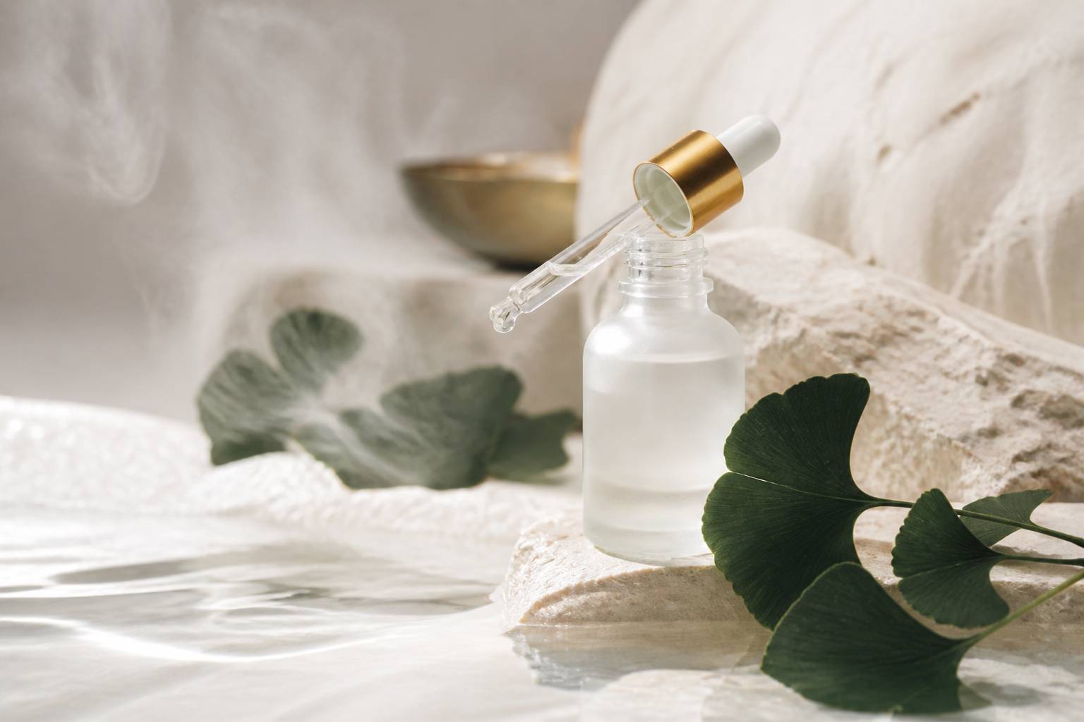 Flacon de sérum en verre avec goutte de texture légère et feuille de ginkgo